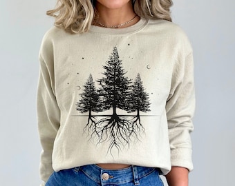 Peut inclure: Un sweat-shirt beige avec un motif noir de trois arbres avec des racines et des étoiles. Les arbres sont en silhouette sur un fond clair.