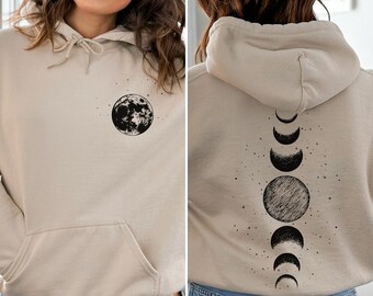 Peut inclure: Un sweat à capuche beige avec un motif de lune noire et d'étoiles sur le devant et un motif de phases de lune noires au dos.