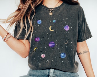 May include: A dark gray t-shirt with a space-themed print featuring planets, moons, and stars in shades of blue, purple, and yellow. The shirt has a relaxed fit and a crew neck.