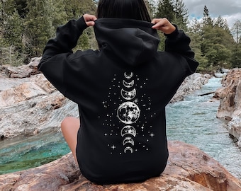 Peut inclure: Sweat-shirt à capuche noir avec un motif de phases de lune blanc au dos. Le motif représente une pleine lune, des croissants de lune et des étoiles.