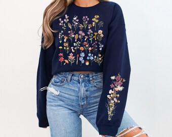Peut inclure: Un sweat-shirt bleu marine court avec un imprimé floral et de champignons. Le sweat-shirt a des manches longues et une coupe décontractée.