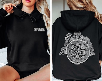 Peut inclure: Sweat-shirt à capuche noir avec un motif blanc représentant une souche d'arbre avec des champignons qui poussent autour. Le texte "Back To My Roots Apparel Co." est imprimé sur le devant du sweat-shirt.