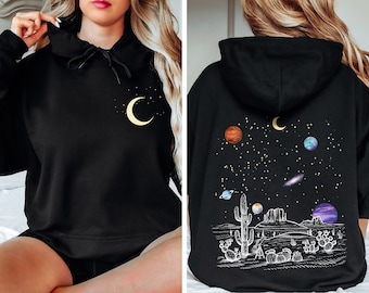 Peut inclure: Sweat-shirt à capuche noir avec un croissant de lune et des étoiles sur le devant et un motif de cactus et de planètes au dos.