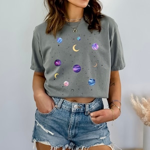 May include: A gray t-shirt with a galaxy print featuring planets, stars, and moons. The shirt is cropped and has a relaxed fit.