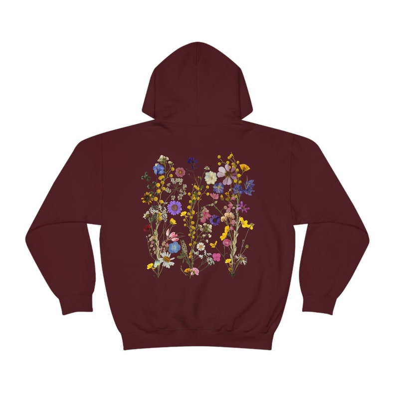 May include: Burgundy hooded sweatshirt with a floral print on the back. The print features a variety of dried flowers in shades of pink, purple, yellow, and blue.