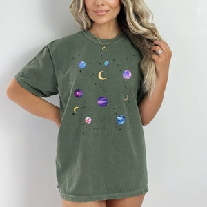 May include: A dark green t-shirt with a celestial print featuring planets, moons, and stars in shades of purple, blue, and yellow.