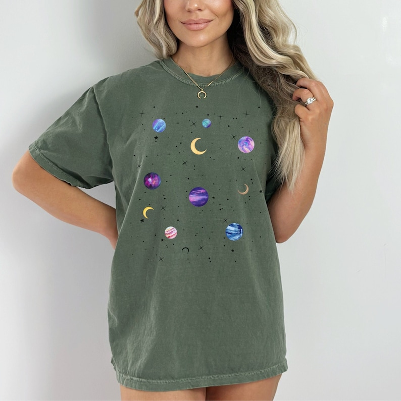 May include: A dark green t-shirt with a celestial print featuring planets, moons, and stars in shades of purple, blue, and yellow.