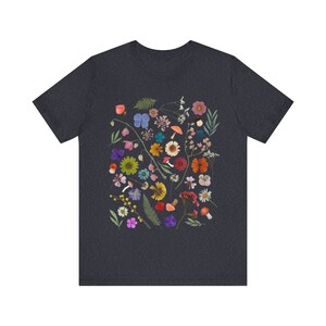 Może przedstawiać: Szary t-shirt w ciemnym odcieniu melanżu z kolorowym nadrukiem kwiatowym przedstawiającym r&oacute;żne kwiaty, liście i grzyby.