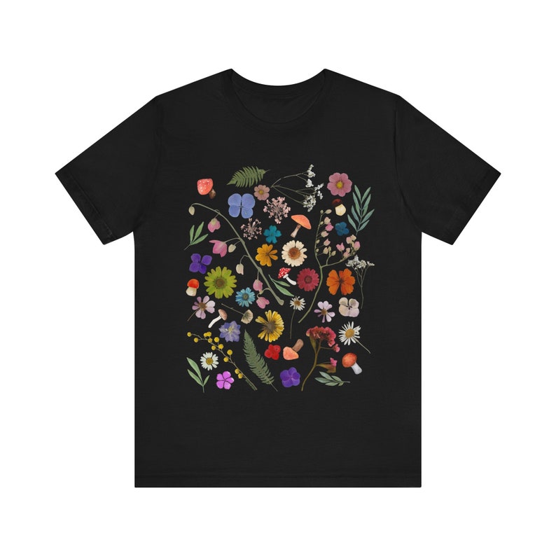 Może przedstawiać: Czarny T-shirt z kolorowym nadrukiem kwiatowym przedstawiającym r&oacute;żne kwiaty, liście i grzyby.