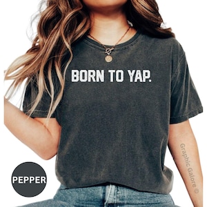 May include: A dark gray t-shirt with the text "BORN TO YAP." printed in white.