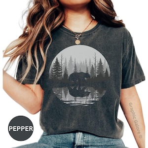 May include: Dark gray t-shirt featuring a circular graphic of a bear in a forest scene reflected in water. The design is in shades of gray and white. The word "Pepper" is in a circle at the bottom left.