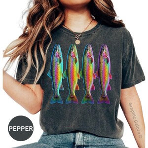 May include: A charcoal gray short-sleeve t-shirt featuring a graphic print of four rainbow trout arranged in a row. Each fish displays a vibrant, multi-colored gradient pattern with shades of blue, green, yellow, and pink. The shirt has a crew neckline.