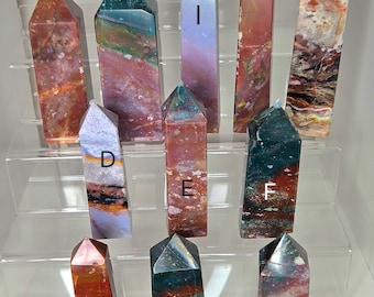 May include: Eleven polished, pointed, multi-colored agate crystal wands, labeled A through K, arranged in three rows on a clear acrylic display stand.
