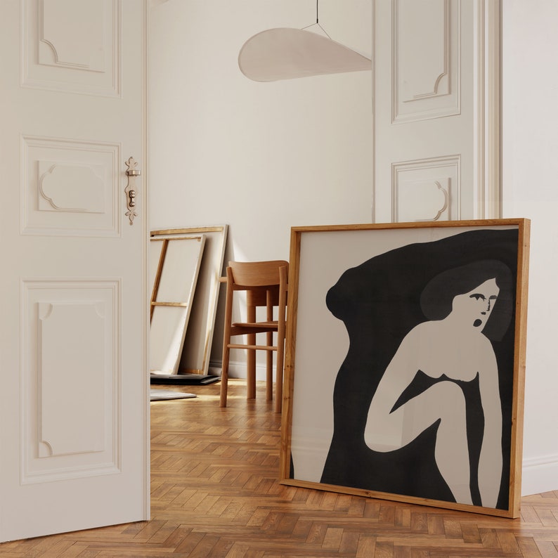 May include: A framed black and white illustration of a woman with a dark shadow behind her. The illustration is set against a light beige background.