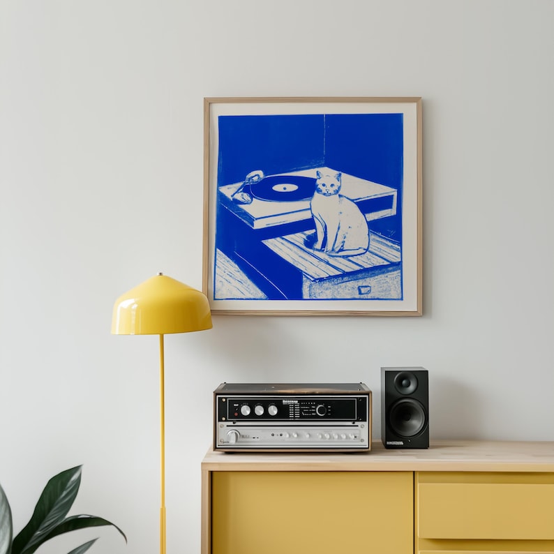 Framed print in Blue and White of a Cat sitting next to a record player. The Framed Print sits above a yellow record player console.