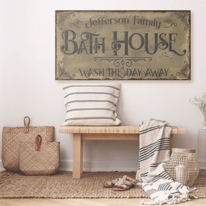 May include: A rustic wooden sign with the text "Jefferson Family Bath House Wash the Day Away" in black lettering on a beige background.