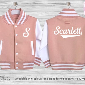 May include: A pink and white baseball style jacket with a white letter 'S' on the front and the name 'Scarlett' in a white baseball font on the back.