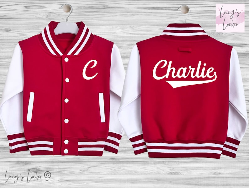 May include: A red and white varsity jacket featuring a white letter C on the front left chest and the name Charlie printed in white script on the back. The jacket has white sleeves, a striped collar, cuffs, and hem, with white snap button closures.