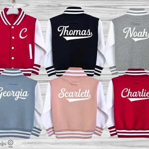 May include: Six varsity jackets in red, navy, grey, blue, pink, and maroon with white sleeves. The jackets feature white striped ribbed collars, cuffs, and hems. Five jackets display white names on the back, while one red jacket shows a white letter C.