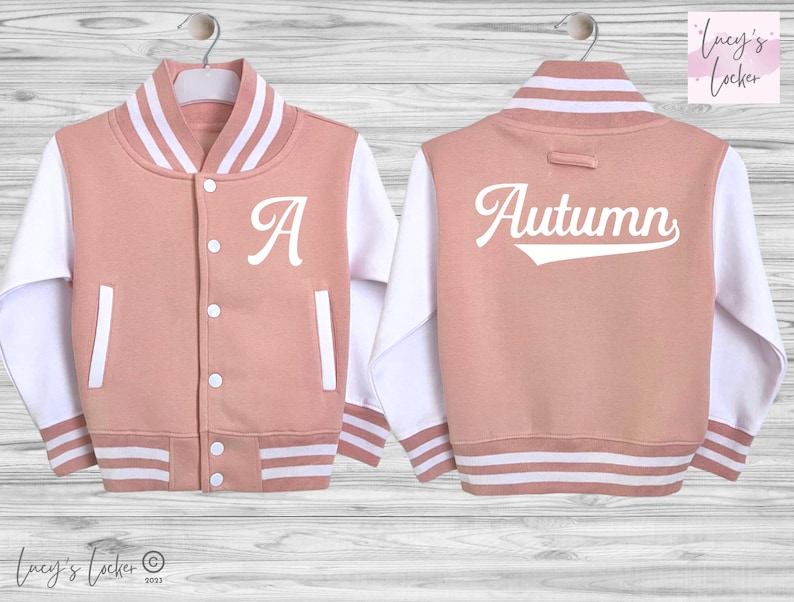 May include: A dusty rose varsity jacket with white sleeves, featuring a white letter A on the front left chest and the name Autumn in white script on the back. The jacket includes a snap-button front, white striped ribbed trim, and pockets.