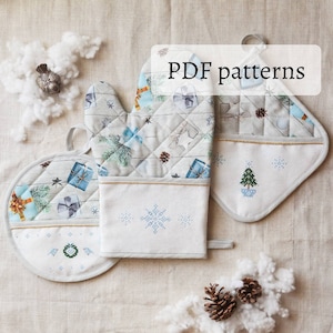 Puede incluir: Tres agarraderas de olla acolchadas blancas y azules con un diseño invernal. Las agarraderas presentan un copo de nieve, un árbol de Navidad y un patrón de regalos y ramas de pino. El texto "PDF patterns" está escrito en blanco sobre un rectángulo blanco.