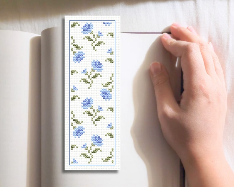 May include: A blue and green cross-stitch bookmark with a floral pattern. The bookmark is rectangular and has a white background.