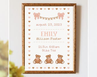 May include: Cross-stitch birth announcement framed in a gold-colored frame. The announcement includes the name "Emily", birth date, time, length (21.5in), and weight (9lbs 7oz). The design features hearts, bows, and teddy bears.
