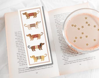 May include: A bookmark with a cross-stitch design of five dachshund dogs in different colors and patterns. The bookmark is white with a brown border.