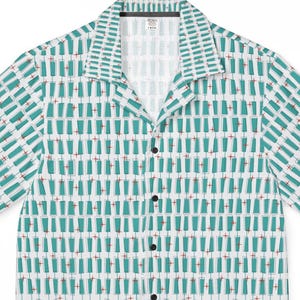 May include: A short-sleeve button-down shirt with a camp collar, featuring a repeating pattern of teal-colored cocktail glasses with small red garnishes on a white background. The shirt has a front button placket with five visible black buttons.