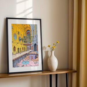 May include: A framed print of a colorful illustration depicting a yellow and gray building with a blue circular detail in the center. The building has a series of arches and windows. The print is hanging on a wooden shelf with a white vase and yellow flowers.