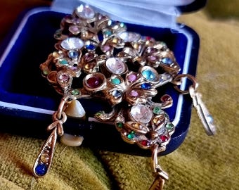 Opvallende vintage kroonluchterbroche met gefacetteerde, transparante strass-steentjes en goudkleurige accenten. Broche in rococo-barokstijl met strass-steentjes.
