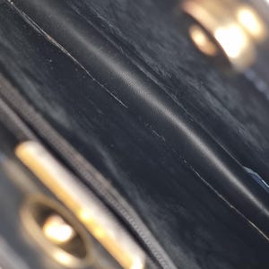 May include: Close-up of the interior of a black leather handbag. The image shows the textured leather, stitching, and a gold-colored clasp. The bag appears to be vintage or pre-owned, with visible wear and tear.