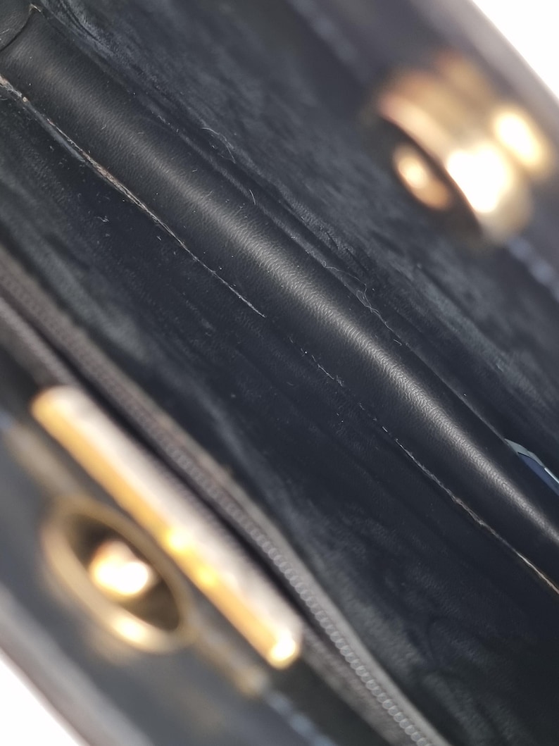 May include: Close-up of the interior of a black leather handbag. The image shows the textured leather, stitching, and a gold-colored clasp. The bag appears to be vintage or pre-owned, with visible wear and tear.