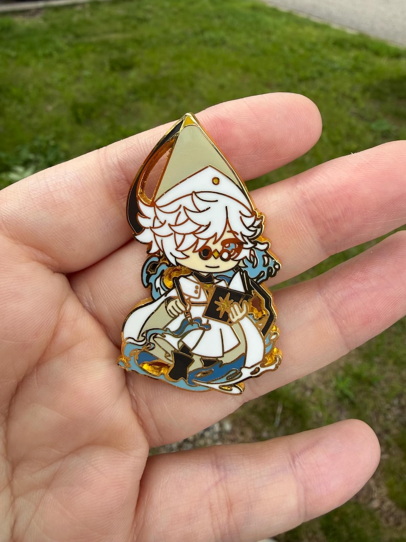 May include: A gold-toned metal enamel pin featuring a stylized character with white hair, wearing a pointed hat and white robes, holding an open book with a gold star emblem, surrounded by blue wave-like patterns and gold outlines.