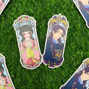 May include: Several stickers featuring anime-style illustrations of characters in traditional Asian attire. The stickers have a rectangular shape with ornate decorative borders. The characters are depicted with detailed facial features and colorful clothing.