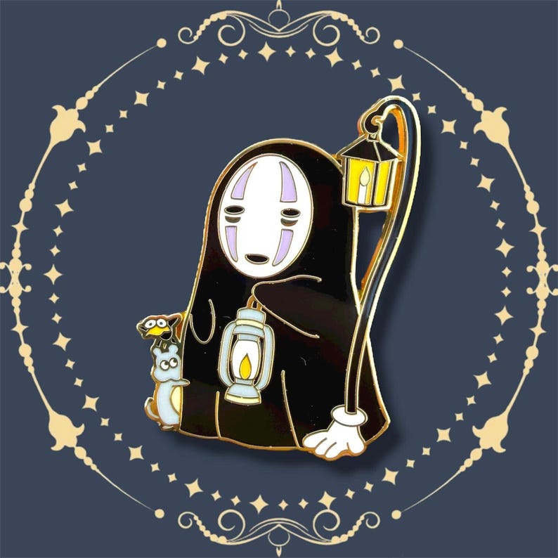 K&ouml;nnte beinhalten: Ein schwarzer Emaille-Pin mit einer Figur aus Spirited Away, die zwei Laternen h&auml;lt. Die Figur hat ein wei&szlig;es Gesicht mit lila Akzenten und eine kleine blaue Kreatur. Der Pin hat goldfarbene Metallakzente.