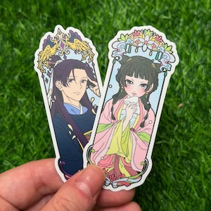 May include: Two stickers featuring anime-style illustrations of characters in traditional Asian attire. One sticker depicts a person in a blue and purple outfit, while the other shows a person in a pink and yellow outfit. Both stickers have decorative borders.