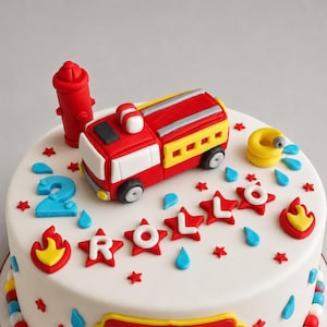 Peut inclure: Un gâteau blanc décoré d'un camion de pompiers rouge et jaune, d'une borne d'incendie rouge et du mot "Rollo" en lettres rouges en forme d'étoile. Le gâteau présente également des gouttes d'eau bleues, des étoiles rouges et le chiffre 2.