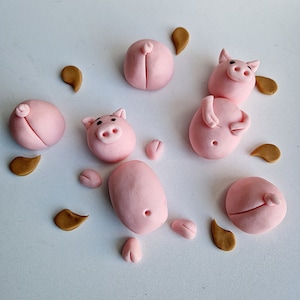 May include: A set of pink fondant pig figurines with brown fondant accents. The pigs are in various poses, including standing, sitting, and lying down. The figurines are perfect for decorating cakes or cupcakes.