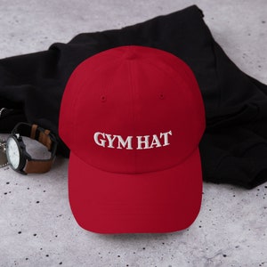 May include: A red baseball cap with a white embroidered design that says "GYM HAT".
