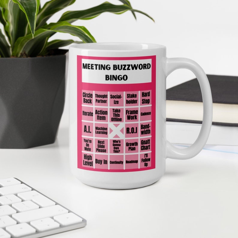 Puede incluir: Una taza de caf&eacute; blanca con un dise&ntilde;o rosa. La taza presenta una tarjeta de bingo con palabras clave comunes de negocios como "circle back", "thought partner", "socialize", "stakeholder", "hard stop", "iterate", "action item", "take this offline", "frame work", "cadence", "A.I.", "machine learning", "R.O.I", "bandwidth", "you're on mute", "next slide please", "who's gonna own this", "growth plan", "gnatt chart", "high level", "buy in", "continuity", "roadmap", y "I'll follow up".