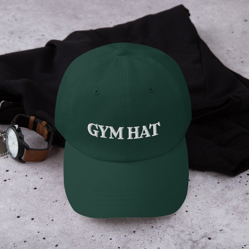 May include: A dark green baseball cap with white embroidery that reads "GYM HAT".