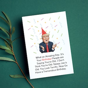 Puede incluir: Una tarjeta de cumpleaños con una ilustración de dibujos animados de una persona con un gorro de fiesta rojo y un traje. El texto de la tarjeta dice "What an Amazing Day. It's Your Birthday! People are Saying You're Old, I Don't Think You're Old. Sleepy Joe is Old. You Look Terrific. Now Go Have a Tremendous Birthday."