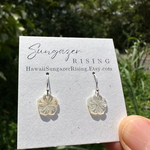May include: A pair of flower-shaped earrings with a pearlescent finish, hanging from silver hooks. The earrings are displayed on a white card with the text "Sungazer Rising" and the Etsy shop URL.