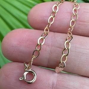 May include: A gold chain necklace extender with a lobster clasp and a heart-shaped charm. The charm has the word "love" engraved on it.