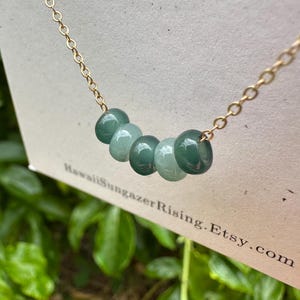 May include: A gold chain necklace with five round, green glass beads. The beads are graduated in size, with the largest bead in the center.