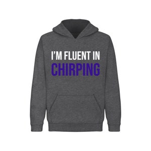 May include: A dark gray hooded sweatshirt with the text "I'M FLUENT IN CHIRPING" printed on the front. The text is in white with the word "CHIRPING" in purple.