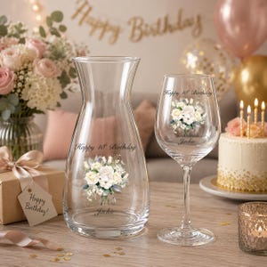 May include: A clear glass carafe and a matching wine glass, both featuring a printed floral bouquet and the text Happy 18th Birthday and Jackie. The carafe has a tapered neck and wide base, while the wine glass has a slender stem and base.