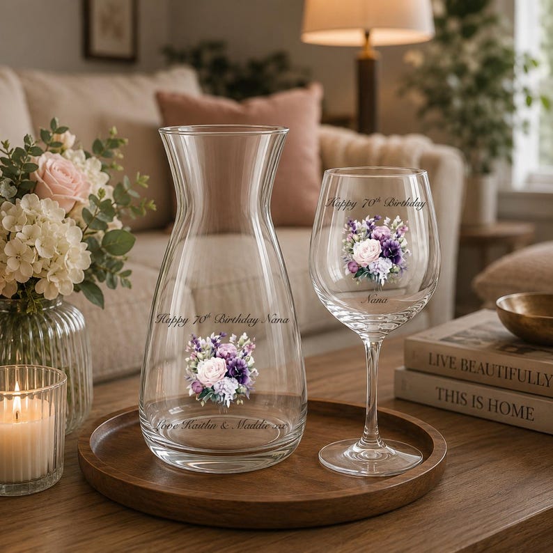 May include: A clear glass carafe and a matching wine glass, both featuring a floral bouquet graphic and the text "Happy 70th Birthday Nana" and "Love Kaitlin & Maddie xo". The items are displayed on a round wooden tray, showcasing elegant designs.
