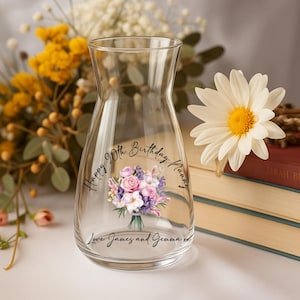Pode incluir: Um vaso de vidro transparente com um design de buqu&ecirc; floral e o texto "Happy 90th Birthday Nanny, Love James and Gemma xx". O vaso &eacute; cercado por flores e livros.